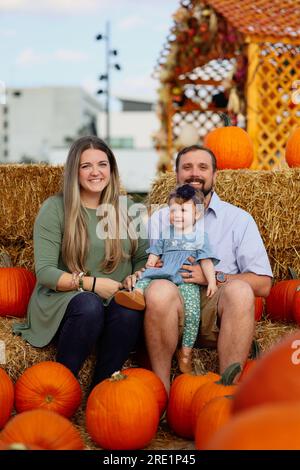 Happy Halloween and Thanksgiving - eine lächelnde Familie und eine kleine Tochter im Hintergrund orangefarbener Kürbisse im Urlaub Stockfoto