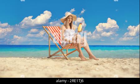 Frau sitzt auf einem Liegestuhl und trägt Sonnencreme auf die Beine am Meer Stockfoto