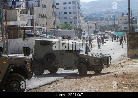 Nalus, Palästina. 24. Juli 2023. Die Palästinenser werfen während einer Militäroperation im Lager östlich von Nablus im besetzten Westjordanland Steine auf die gepanzerten Fahrzeuge des israelischen Militärs. Die israelische Armee hat während einer gemeinsamen Operation zur gleichzeitigen Verhaftung gesuchter Personen die Nour Shams-Lager östlich von Tulkarm und Aqabat Jabr in Jericho, Askar, östlich von Nablus überfallen. Kredit: SOPA Images Limited/Alamy Live News Stockfoto