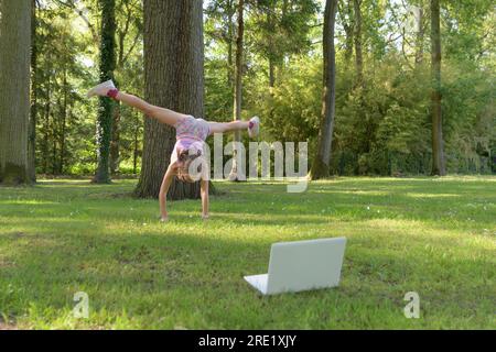 Ein Teenager, das im Park Handstand-Übungen macht. Führt Übungen online mit einem Computer durch Stockfoto