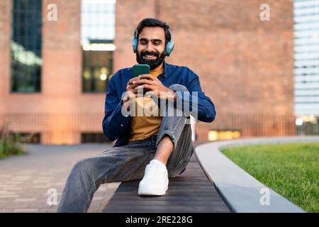 Ein indischer Mann mit Kopfhörern, der draußen am Telefon Musik hört Stockfoto
