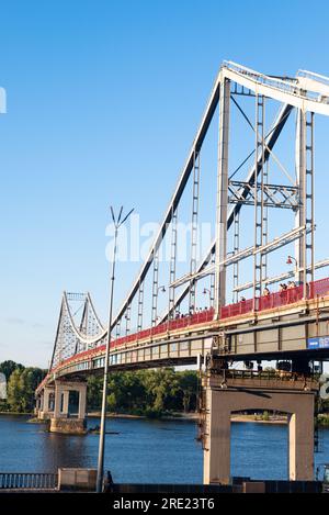 Parken Sie die Fußgängerbrücke über den Dnieper, die den zentralen Teil von Kiew mit dem Parkbereich verbindet. Kiew, Ukraine - 21. Juli 2023 Stockfoto