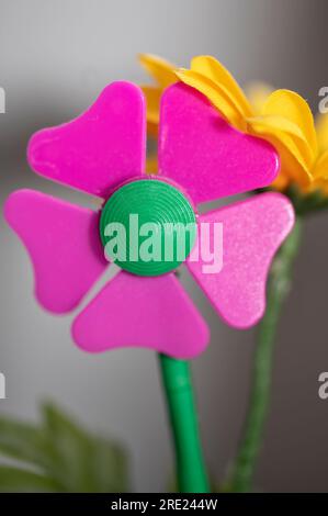 Nahaufnahme einer rosa Blume aus Kunststoff mit einer gelben Blume aus Stoff dahinter Stockfoto