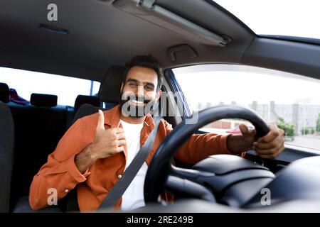 Ein glücklicher araber, der Auto fährt und den Daumen nach oben zeigt, wenn er drinnen sitzt Stockfoto