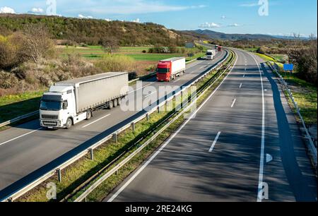 Straßenverkehr. Transportwagen in Schlangen, die auf einer Landstraße unter einem wunderschönen blauen Himmel vorbeifahren Stockfoto