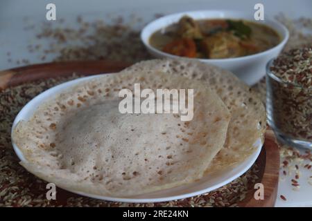 Rajamudi-Reis-Appam serviert mit kerala-Hühnchen-Curry. Reiscrepes oder Pfannkuchen mit fermentiertem Ramamudi-Reisteig und Kokosmilch. Eine Version von Stockfoto