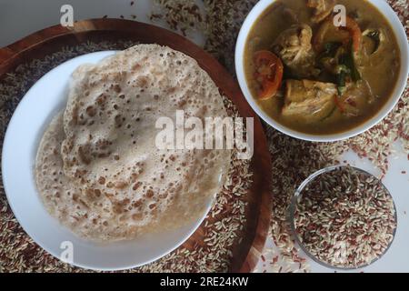 Rajamudi-Reis-Appam serviert mit kerala-Hühnchen-Curry. Reiscrepes oder Pfannkuchen mit fermentiertem Ramamudi-Reisteig und Kokosmilch. Eine Version von Stockfoto