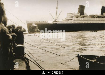 Southampton, Hampshire. c.1938 – am Kai versammeln sich Menschenmassen, um dem transatlantischen Passagierschiff der Cunard-White Star Line, RMS Queen Mary, beim Manövrieren aus den Southampton Docks mit einem Schlepper zuzusehen. Das Schiff wurde von John Brown & Company in Clydebank, Schottland, gebaut und segelte auf ihrer Jungfernfahrt am 27. Mai 1936. Abgesehen von einer Zeit während des Zweiten Weltkriegs, als sie konvertiert und als Truppenschiff angestellt wurde, blieb sie bis 1967 im Dienst. Sie gewann den Blue Riband-Preis für die schnellste transatlantische Überquerung im August 1936 und dann erneut im Jahr 1938, wobei sie ihn bis 1952 behalten hat. Stockfoto