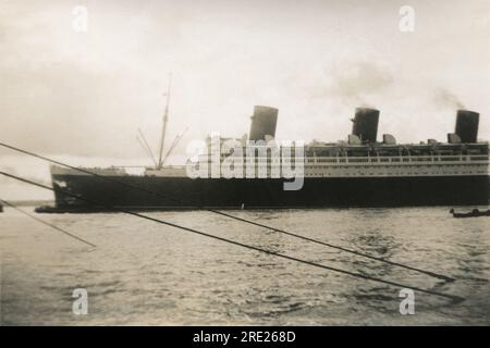 Southampton, Hampshire. c.1938 – das transatlantische Passagierschiff der Cunard-White Star Line, RMS Queen Mary, wird von einem Schlepper aus den Southampton Docks manövriert. Das Schiff wurde von John Brown & Company in Clydebank, Schottland, gebaut und segelte auf ihrer Jungfernfahrt am 27. Mai 1936. Abgesehen von einer Zeit während des Zweiten Weltkriegs, als sie konvertiert und als Truppenschiff angestellt wurde, blieb sie bis 1967 im Dienst. Sie gewann den Blue Riband-Preis für die schnellste transatlantische Überquerung im August 1936 und dann erneut im Jahr 1938, wobei sie ihn bis 1952 behalten hat. Stockfoto