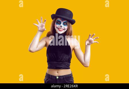 Glückliches Mädchen in schwarzem Kostüm und Hexenhut mit kreativem Schädel-Make-up hat Spaß auf der Halloween-Party. Stockfoto