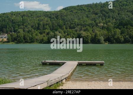 Eine ruhige Szene am Fuße des Happurger Sees, Deutschland, mit einem malerischen hölzernen Pier, der sich in das friedliche Wasser erstreckt. Stockfoto