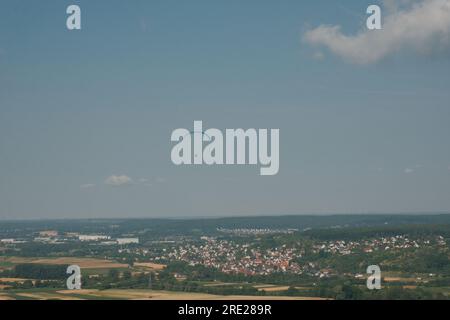 Ein gewagter Gleitschirm schwingt hoch über die malerische deutsche Landschaft, mit einer malerischen Stadt im Hintergrund. Stockfoto