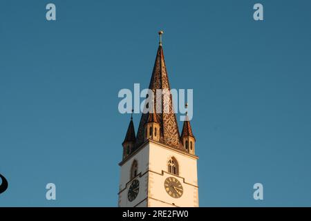 Eine Nahaufnahme eines rumänischen Uhrenturms, gebadet in Sonnenlicht. Das Foto zeigt die komplexen architektonischen Details und den historischen Charme des Bauwerks Stockfoto