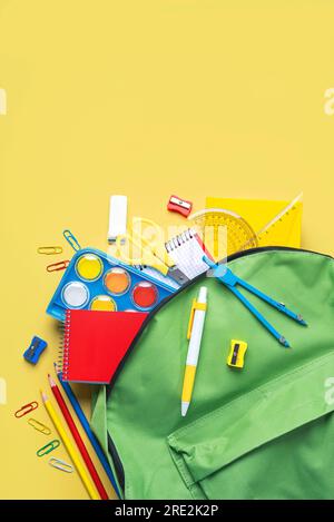 Draufsicht auf Schulrucksack und Schulzubehör mit Platz für Text auf gelbem Hintergrund. Wieder-in-die-Schule-Konzept Stockfoto