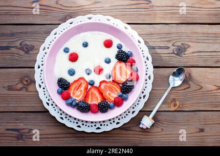 Griechische Joghurtschüssel mit frischen Beeren, Erdbeeren, Himbeeren, Heidelbeeren auf natürlichem Holzhintergrund, Draufsicht Stockfoto