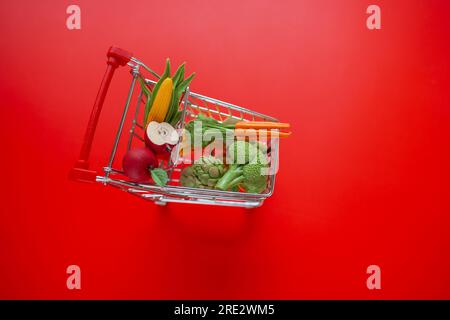 Warenkorb mit Lebensmitteln auf einem roten background.grocery-cm-Warenkorb. Lebensmittelkosten. Preiserhöhung für Gemüse und Obst. Supermarkt Trolley mit Stockfoto