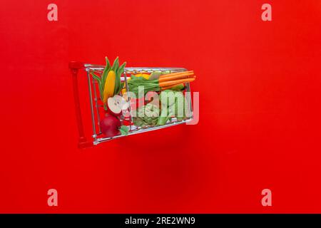 Essenskosten. Einkaufswagen mit Lebensmitteln auf einem roten background.grocery-cm-Warenkorb. Preiserhöhung für Gemüse und Obst. Dekorativer Supermarkt Stockfoto