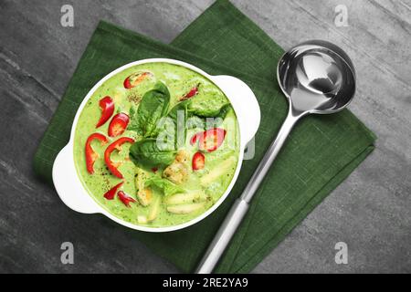 Kochtopf mit leckerer grüner Curry-Hühnersuppe und Schöpfkelle auf hellgrauem Tisch, flach liegend Stockfoto