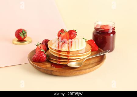 Teller mit leckeren Pfannkuchen mit süßer Erdbeermarmelade auf beigefarbenem Hintergrund Stockfoto