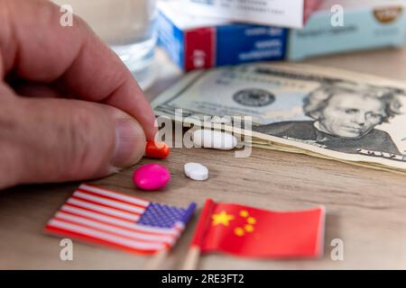 Ein Pharma-, Medizin- und Drogenkonflikt-Konzept mit den amerikanischen und chinesischen Flaggen, US-Dollar-Rechnungen und verschiedenen Medikamenten auf einem Schreibtisch. Stockfoto