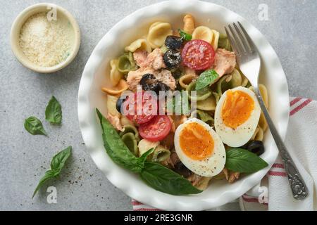 Italienischer Nudelsalat. Orekchiette-Pasta mit Thunfisch, Tomatenkirsche, Oliven, Basilikum und Parmesan auf grauem Stein- oder Betonhintergrund. Rz Stockfoto