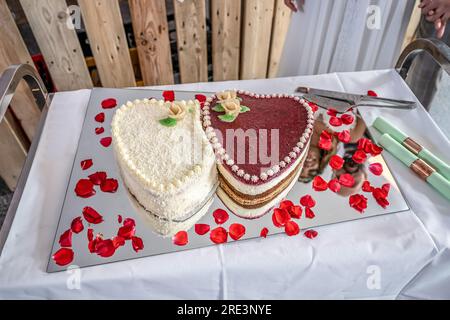 Romantische Hochzeit zwei Kuchen in Herzform, Rosenstrauß auf weißem Tischhintergrund. Draufsicht. Stockfoto