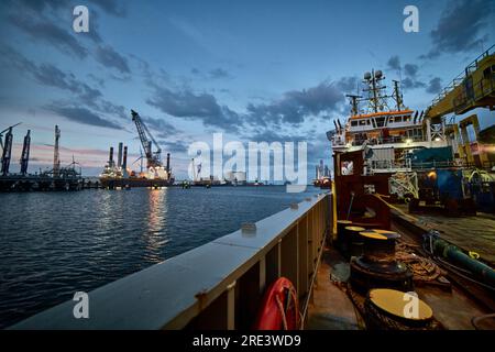 Blick auf den Sonnenuntergang vom Schiff im Hafen mit Windturbinen am Horizont. Stockfoto