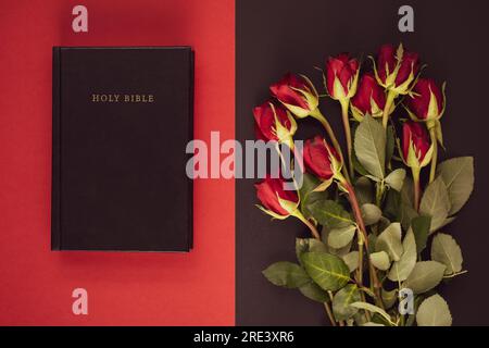 Heilige Bibel und rote Rosen auf schwarzem und rotem Hintergrund. Christliches Konzept, Kopierraum Stockfoto