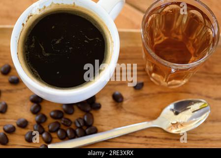 Schwarzer Kaffee und heißer Tee auf einem Holztisch mit Kaffeebohnen und einem Löffel Stockfoto