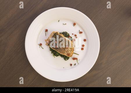 Gegrillter Fisch und Spinat auf einem Holztisch Stockfoto