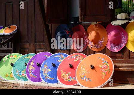 Handgefertigte Schirme und farbenfrohe Hüte vor dem Hintergrund des Holzhauses Stockfoto