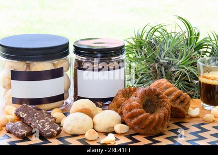 Macadamianüsse und Kekse in einer Plastikbox neben einer Tasse schwarzen Kaffees auf einem Holztisch im Garten Stockfoto