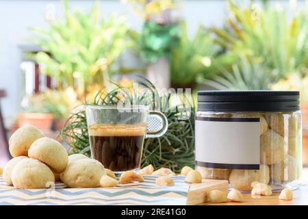 Macadamianüsse und Kekse in einer Plastikbox neben einer Tasse schwarzen Kaffees auf einem Holztisch im Garten Stockfoto