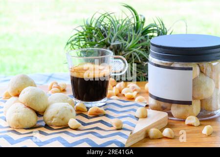 Macadamianüsse und Kekse in einer Plastikbox neben einer Tasse schwarzen Kaffees auf einem Holztisch im Garten Stockfoto