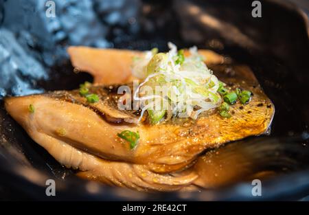 Lachskabutoni, Lachskopf in Sojasoße mit geschnittenen ​​spring-Zwiebeln, serviert in einer schwarzen Schüssel. Stockfoto