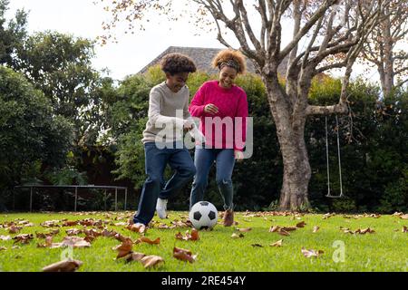 Glückliche afroamerikanische Mutter und Sohn, die im Garten Fußball spielen Stockfoto