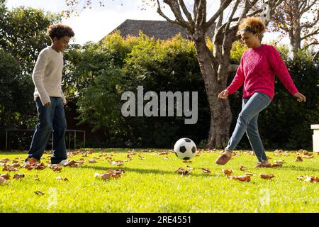 Glückliche afroamerikanische Mutter und Sohn, die im Garten Fußball spielen Stockfoto