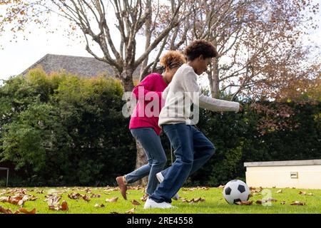 Glückliche afroamerikanische Mutter und Sohn, die im Garten Fußball spielen Stockfoto