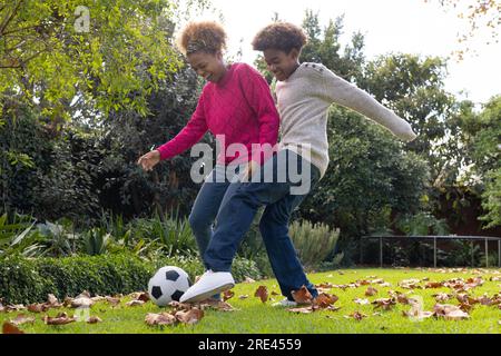 Glückliche afroamerikanische Mutter und Sohn, die im Garten Fußball spielen Stockfoto