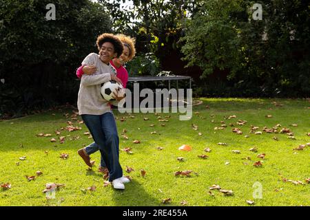 Glückliche afroamerikanische Mutter und Sohn, die im Garten Fußball spielen Stockfoto