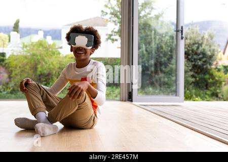 Ein glücklicher afroamerikanischer Junge, der auf dem Boden sitzt, mit einem Headset, Kopierraum Stockfoto