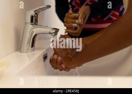 Mittelteil von afroamerikanischer Mutter und Sohn, die sich im Badezimmer die Hände waschen Stockfoto