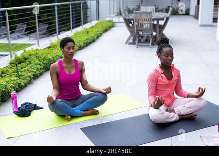 afroamerikanische Mutter und Tochter, die zu Hause Yoga auf der sonnigen Terrasse üben Stockfoto