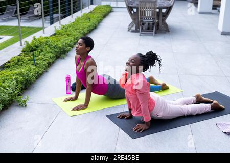 Glückliche afroamerikanische Mutter und Tochter, die zu Hause Yoga auf der sonnigen Terrasse praktizieren Stockfoto