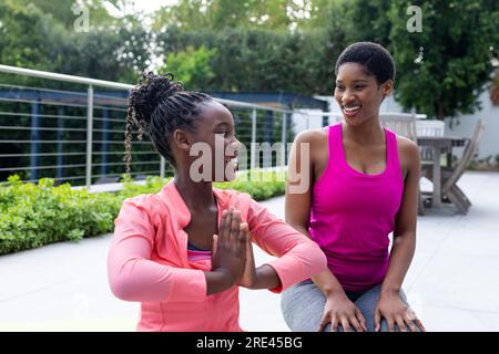 Glückliche afroamerikanische Mutter und Tochter, die zu Hause Yoga auf der sonnigen Terrasse praktizieren Stockfoto