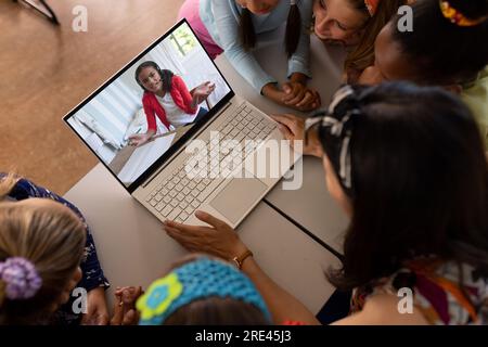 Eine asiatische Lehrerin und verschiedene Schüler, die mit einem Mädchen in der Schule ein Videogespräch auf dem Laptop führen Stockfoto