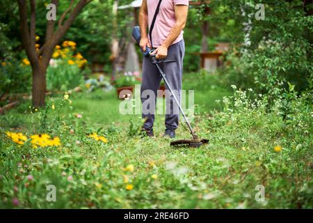 Nahaufnahme eines jungen Mannes, der Gras mit dem Unkrautschneider auf seinem grasbedeckten Rasen mäht. Gartenkonzept Stockfoto