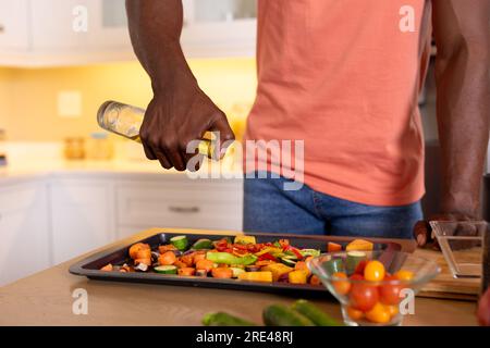 Mittelschnitt eines afroamerikanischen Mannes, der in der Küche Öl auf Gemüse gießt Stockfoto