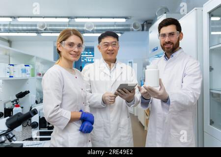 Erfolgreiches Team von Wissenschaftlern, drei Personen Mann und Frau lächeln und schauen in die Kamera, Portrait einer Gruppe von Wissenschaftlern in weißen medizinischen Kitteln in einem Labor. Stockfoto