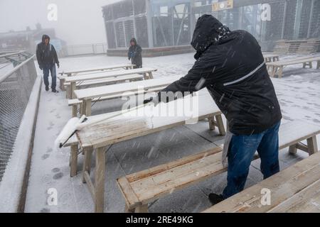 Garmisch Partenkirchen, Deutschland. 25. Juli 2023. Während eines Schneesturms auf der Zugspitze (2962 Meter) entfernt ein Mann Schnee von den Tischen auf der schneebedeckten Aussichtsplattform. Kredit: Peter Kneffel/dpa/Alamy Live News Stockfoto